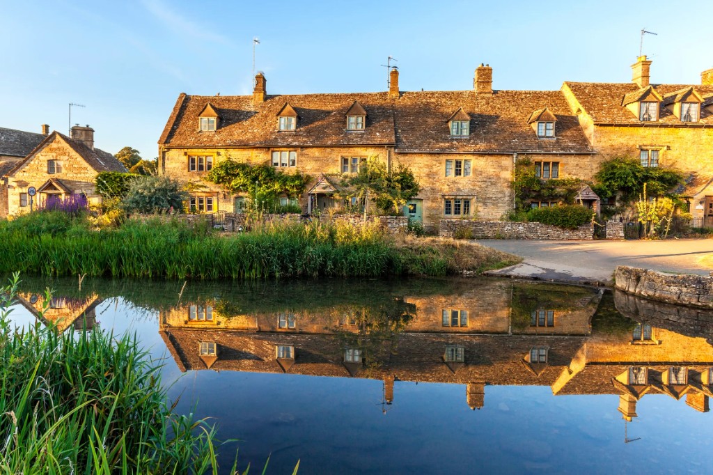 Honey-stone cottages reflected in the river at golden hour
